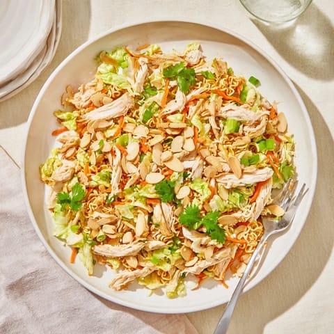 A close-up of Crunchy Ramen Chicken Salad with shredded cabbage, carrots, and toasted almonds tossed in a glossy sesame dressing.