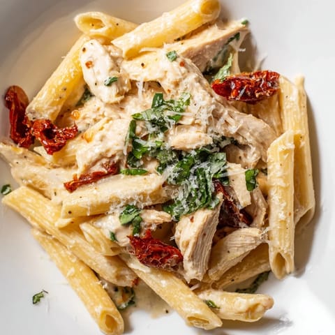 A close-up of Creamy Sun-Dried Tomato Chicken Pasta in a skillet, garnished with fresh basil and melted Parmesan for a comforting Italian-American meal.