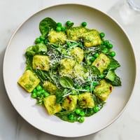 Golden, crispy gnocchi glistens in a skillet, tossed with vibrant green peas and aromatic basil pesto for a comforting vegetarian meal.