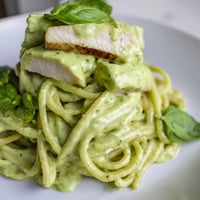 Creamy avocado chicken pasta features grilled chicken slices on silky green sauce over al dente spaghetti, garnished with fresh basil.  